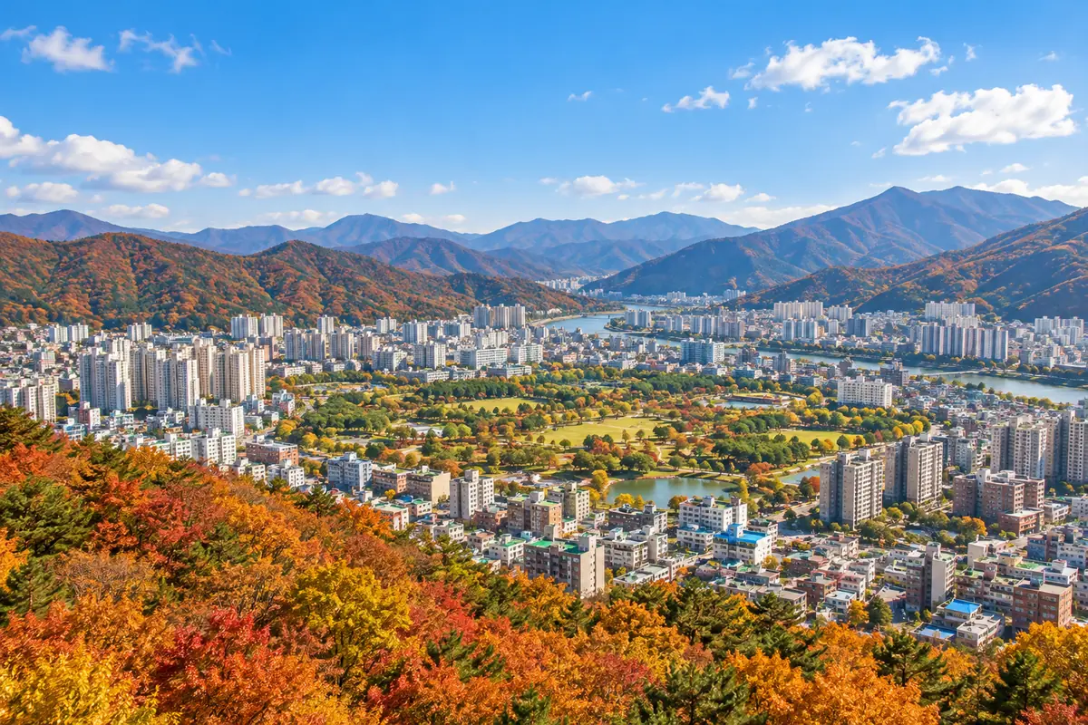 단풍 든 산 능선으로 둘러싸인 분지 도시의 아파트와 녹지, 맑은 가을 하늘