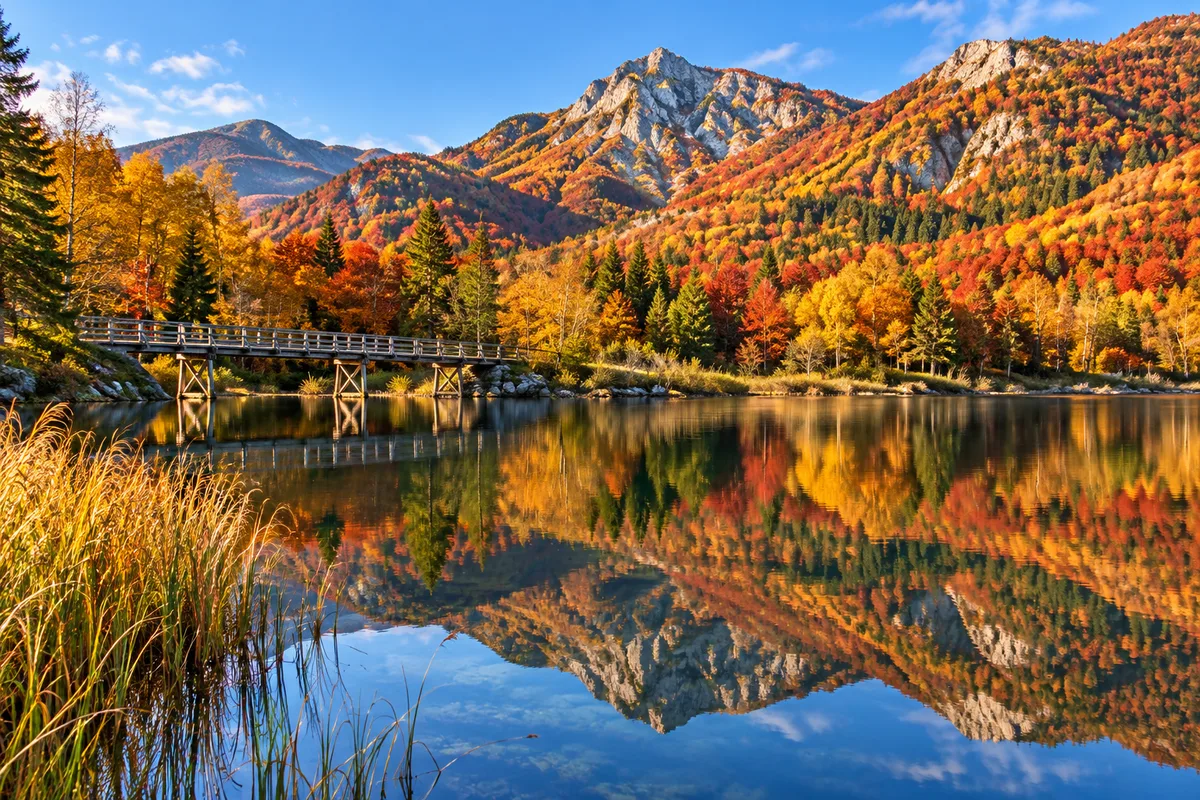 단풍 든 산이 비치는 잔잔한 호수와 물가의 나무 다리, 맑은 가을 오후